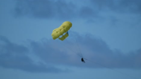 a couple doing parasailing hunging on a yellow parachute in a tropical island