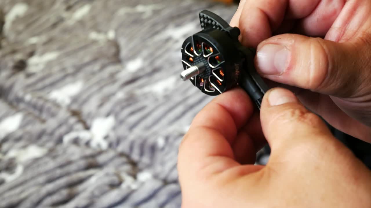 Male hands tighten hobby FPV drone motor onto carbon fibre frame testing strength close up