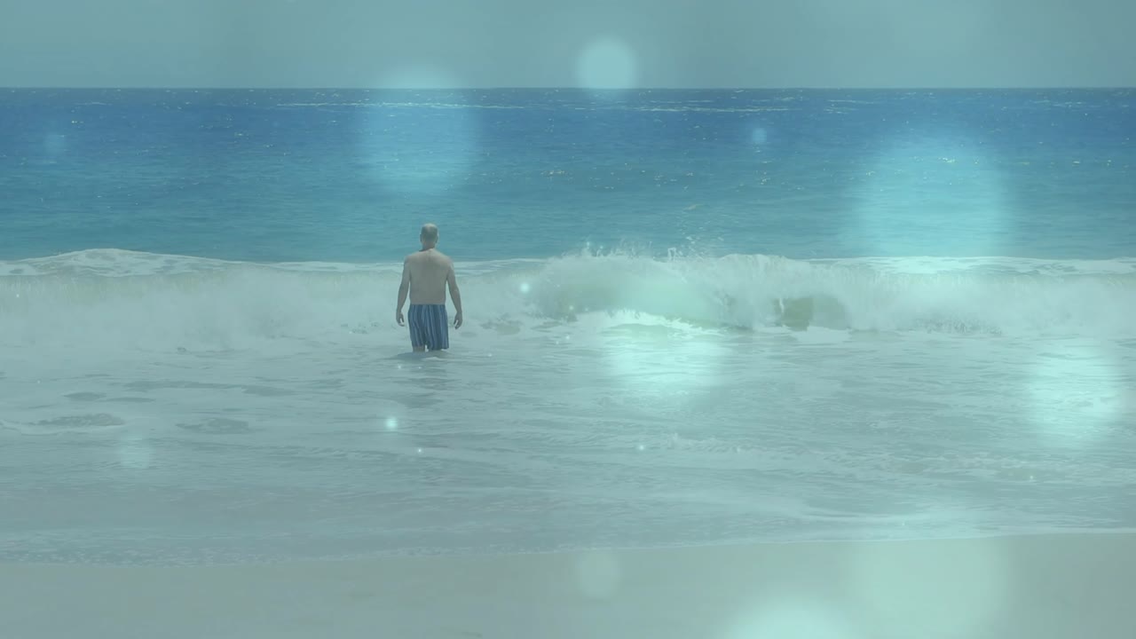 老年男子从岸边涉水进入大海，停顿，海浪拍打，镜头眩光叠加，旅行。