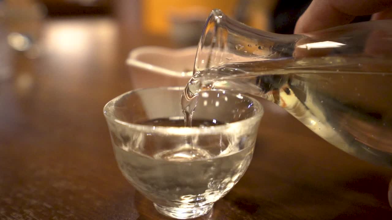 SLOWMO close up of man's hand pouring sake into a cup