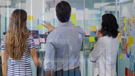 Animation-of-graphs-moving-over-diverse-colleagues-brainstorming-over-sticky-notes-on-glass-wall