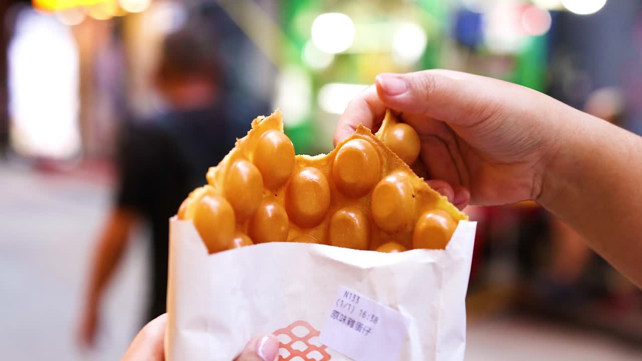 la mano agarrando el waffle de burbuja en una calle concurrida