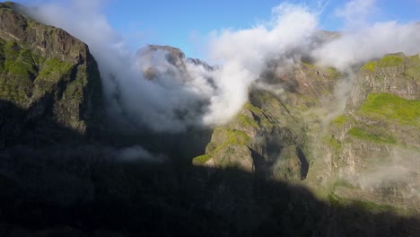 Volando-Sobre-El-Hermoso-Valle-De-Las-Montañas-Rocosas-De-Maderia,-Portugal-Con-Nubes-Tocando-La-Ladera-De-La-Montaña-Con-Una-Vida-Vegetal-Verde-Y-Exuberante-Creciendo---Toma-Aérea