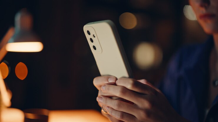 Primo piano di mani che inviano un messaggio da uno smartphone in uno spazio di lavoro buio. Donna non riconoscibile