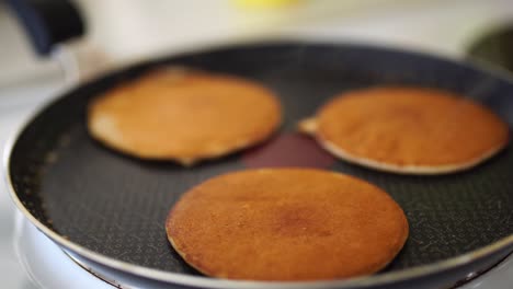 close-up of three golden ruddy pancakes in a frying pan, light white steam.