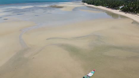 drone video shows traditional small fishing boats anchored near the sandy shoreline of koh phangan, thailand, with clear turquoise water and lush green coastline creating a scenic tropical seascape