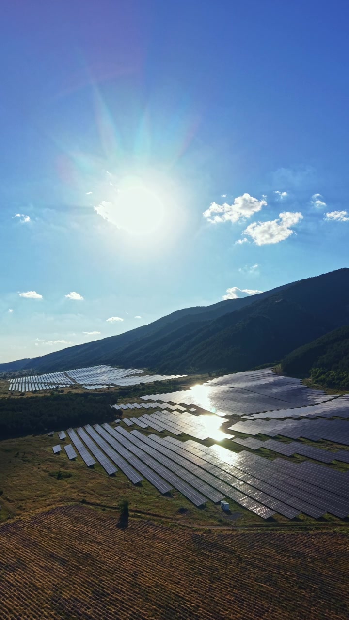 Solpaneler dækker et stort område i en dal under en klar sol med en skyfri himmel og fjerne bjerge om eftermiddagen