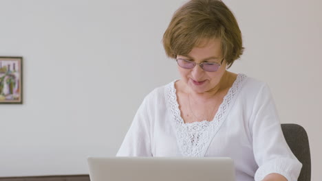 senior woman with eyeglasses sitting on a sofa using tablet