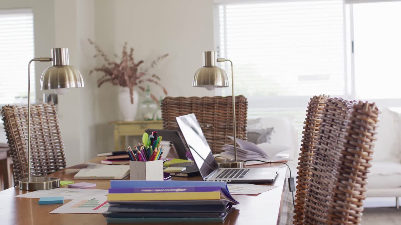 Lamps and laptop on busy desk in home office in dining room, slow motion