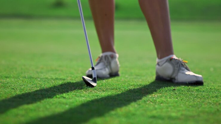 Una donna che fa lo swing con la mazza da golf su un campo in erba. Gambe di donna in posa sul fairway.