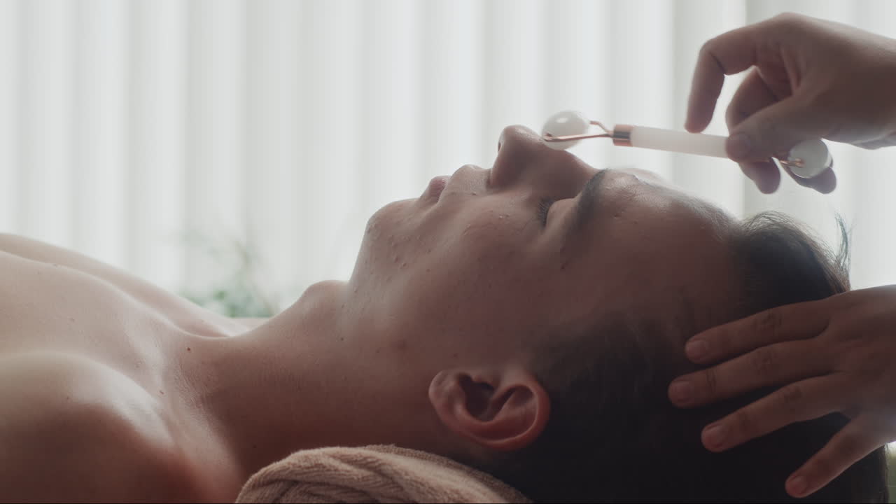 Beautician Doing Facial Massage with Jade Roller to Male Client