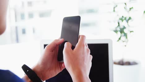 Man-in-office-using-phone-with-laptop-and-wearing-smartwatch