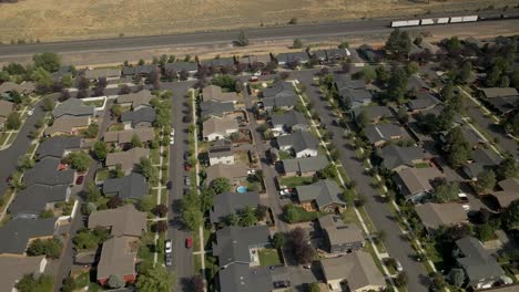 Drone-shot-tilting-up-from-a-suburban-neighborhood-to-the-nearby-train-tracks-cutting-through-Bend,-Oregon