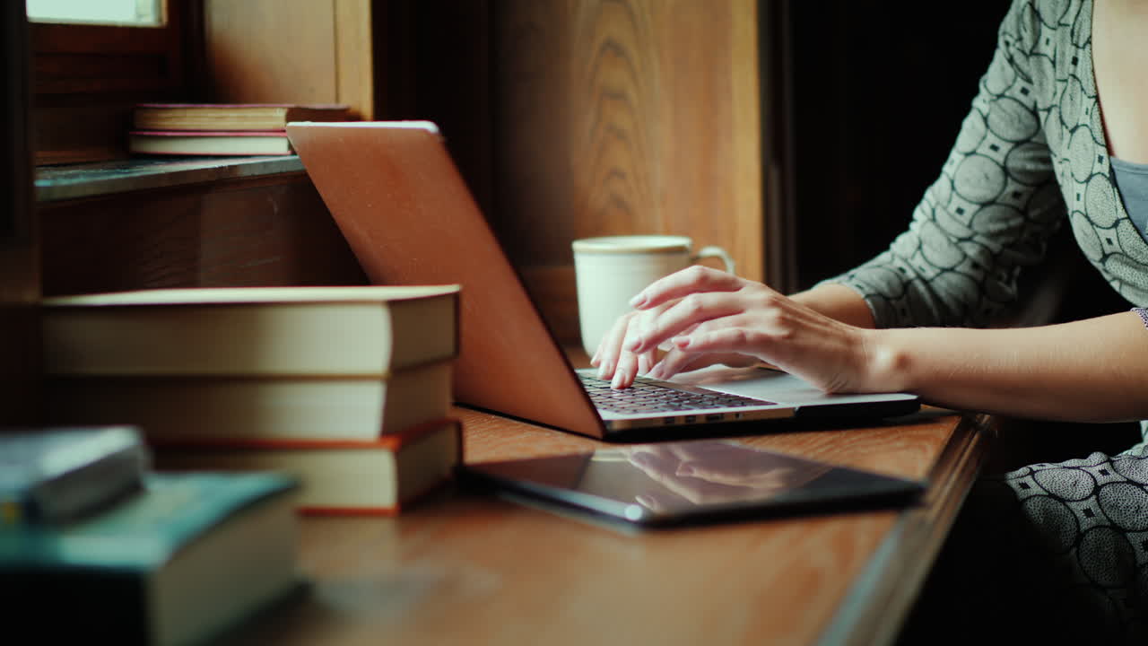Hands Typing on a Laptop With Books Nearby