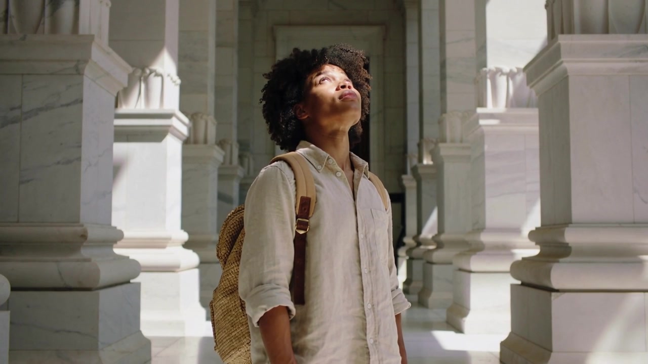 Entering tourist with straw backpack shirt tilting head back looking up to sunlight in marble hall