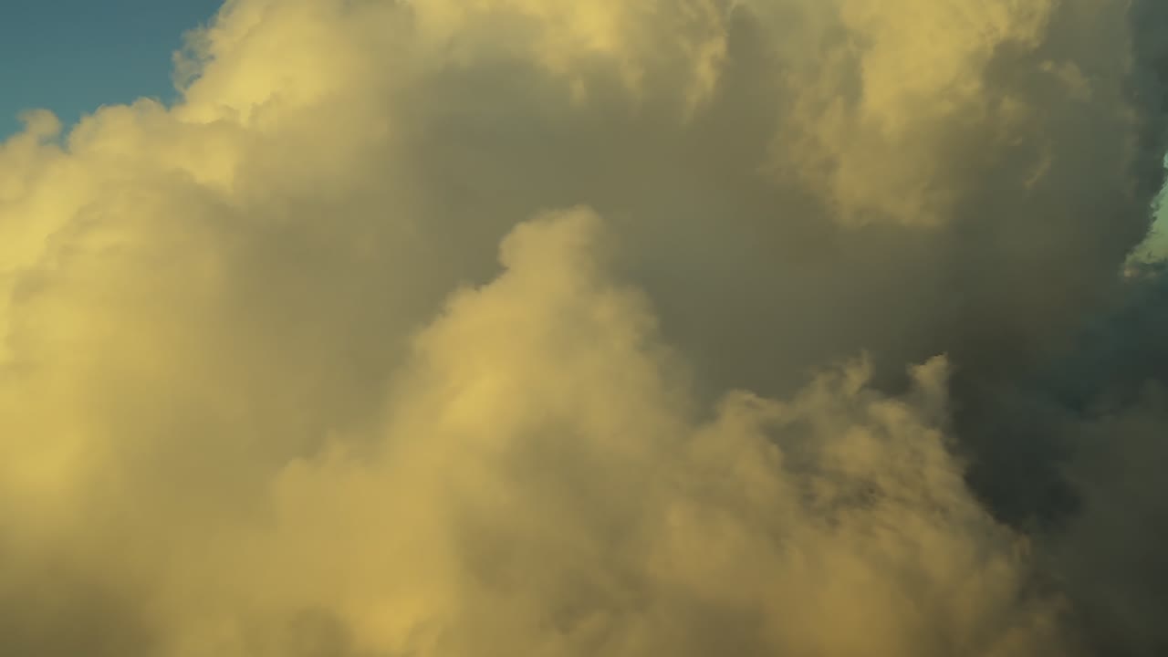 A pilot’s eyes view from a jet ccckpit flying at sunset, with a warm light illuminating cottony golden clouds