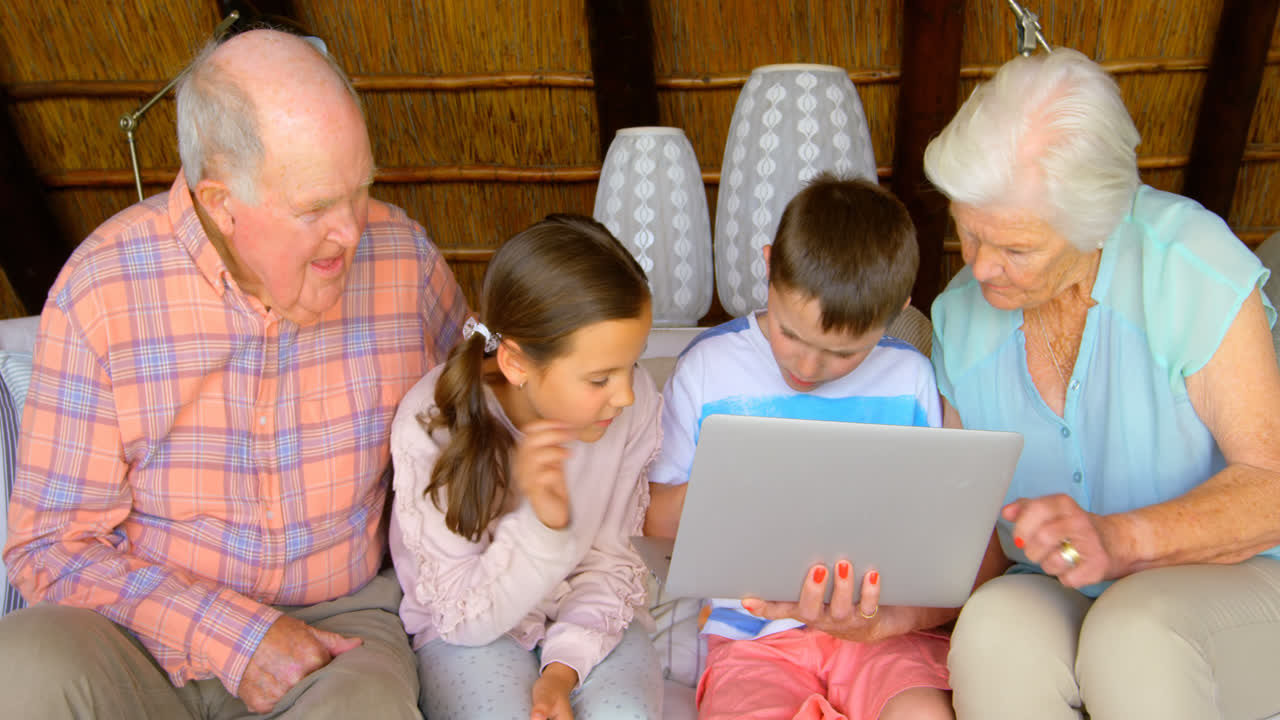 Front view of multi-generation Caucasian family using laptop in a comfortable home 4k