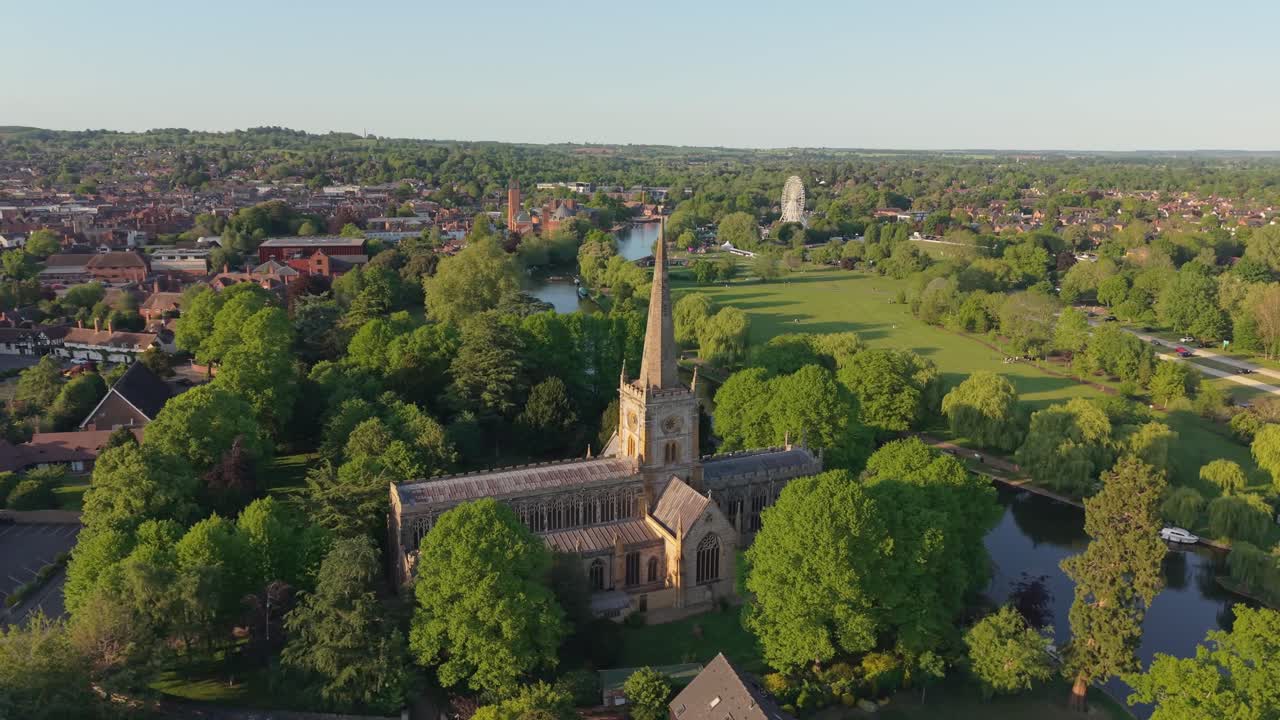 Drone-kierto goottilaisen Pyhän Kolminaisuuden kirkon ympärillä aurinkoisena kevätpäivänä, pyyhkäisten esiin mutkittelevan Avon-joen ja rehevän Stratford-upon-Avonin maiseman taustalla