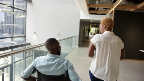 man using wheelchair, business colleagues discussing work while walking in modern office hallway