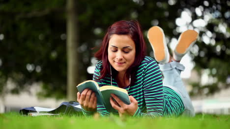 estudiante bonita acostada en la hierba leyendo un libro escuchando música