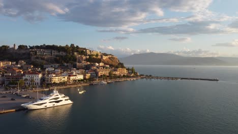 Drone-view-of-the-small-Mediterranean-town-of-Nauplio-in-the-Peloponnese-region-of-Greece,-during-a-cloudy-afternoon-with-yachts-in-port-|-4K