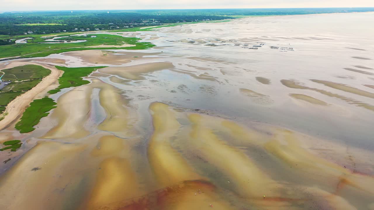 Maine shoreline at low tide reveals natural tidal flats with sand ridges, shallow pools of water reflecting the sky, and scattered dunes rising gently along the open coastline