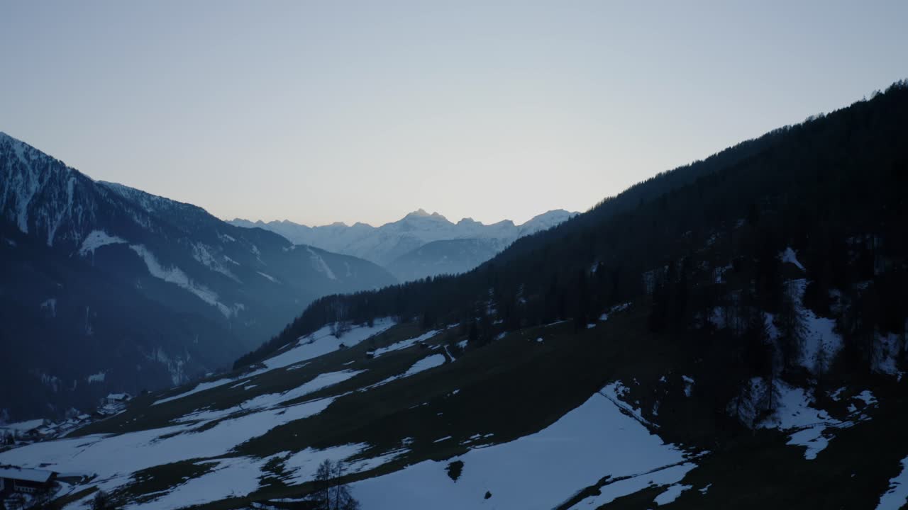 Drone flies over Navistal, Tyrol at sunset—green meadows, white mountain peaks, and patches of spring snow create a stunning contrast in the alpine landscape.