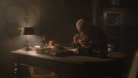older passionate man evaluates an old silver skull watch in his office at night