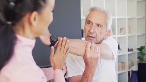 video of happy biracial female physiotherapist exercising with caucasian senior man