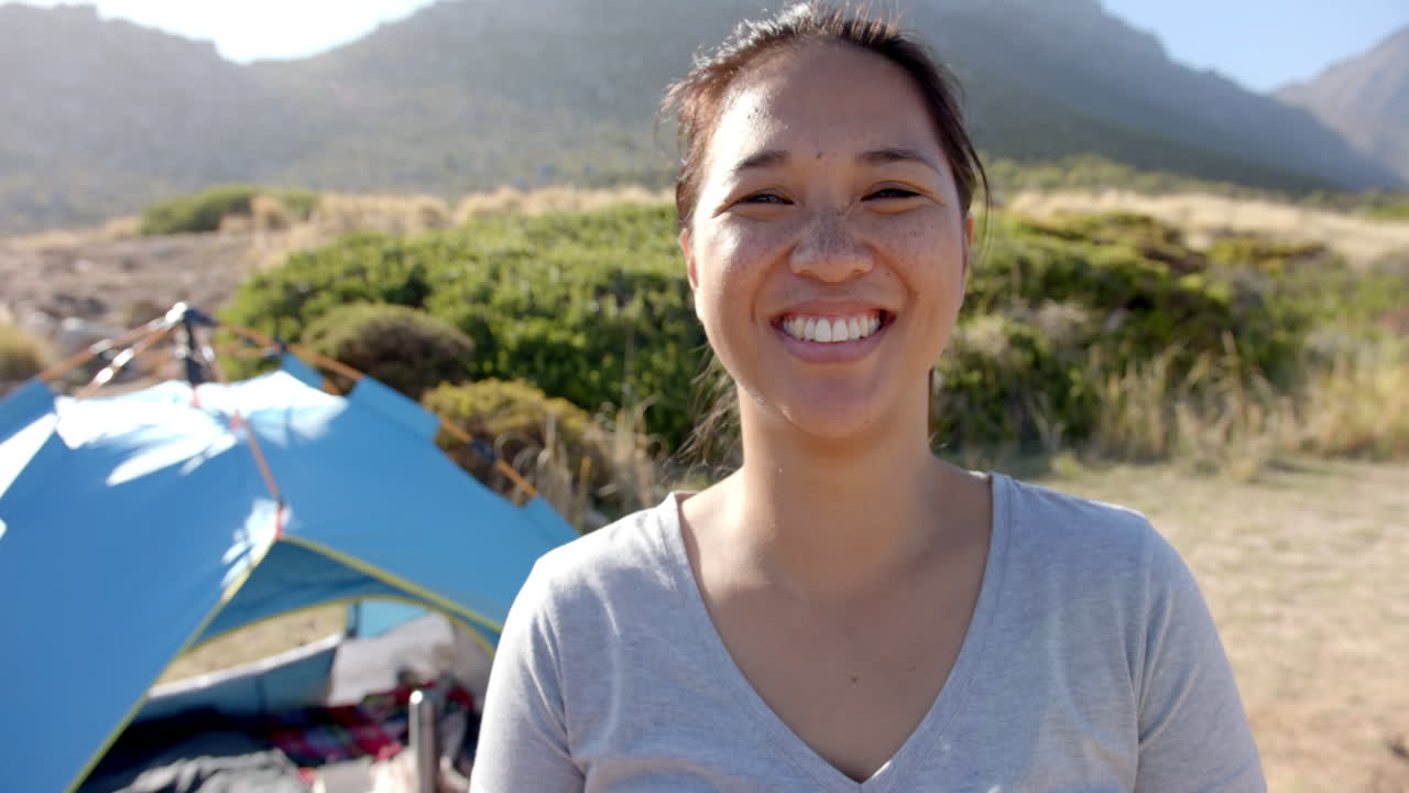 Smiling woman camping near blue tent in scenic mountain landscape
