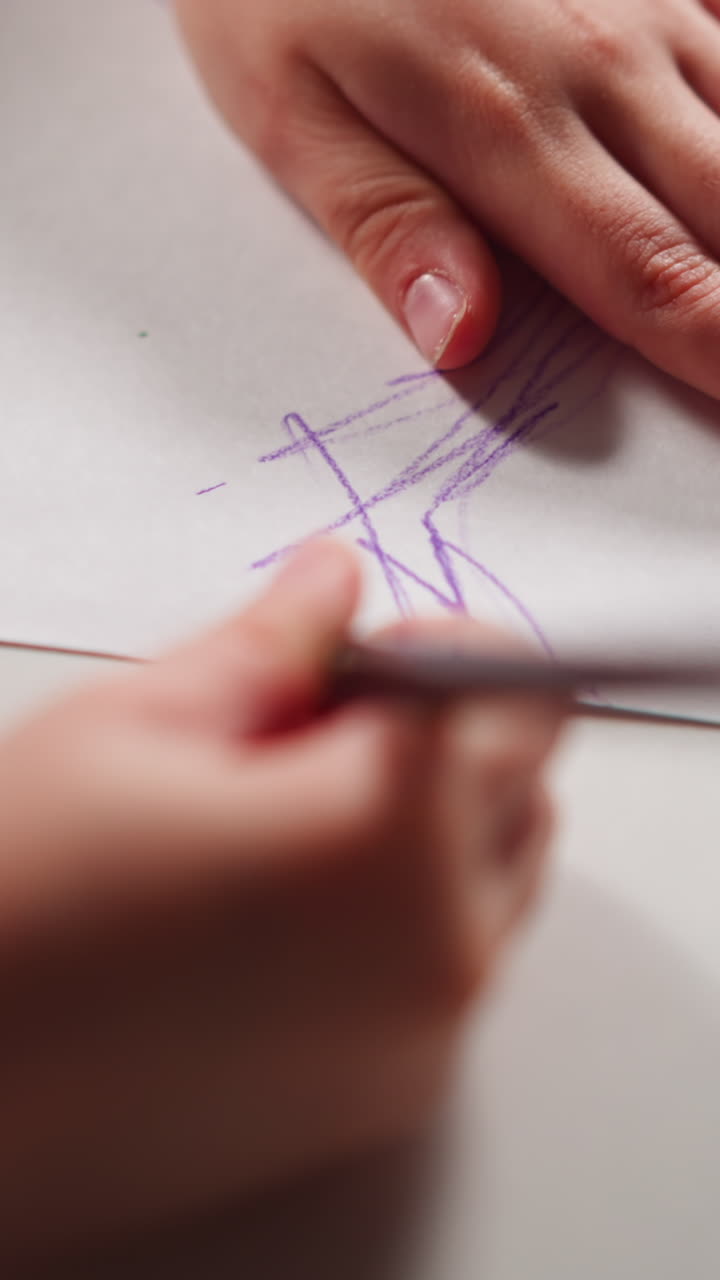 Little girl paints white paper sheet with purple pencil drawing funny sketch at art lesson in children room extreme closeup slow motion