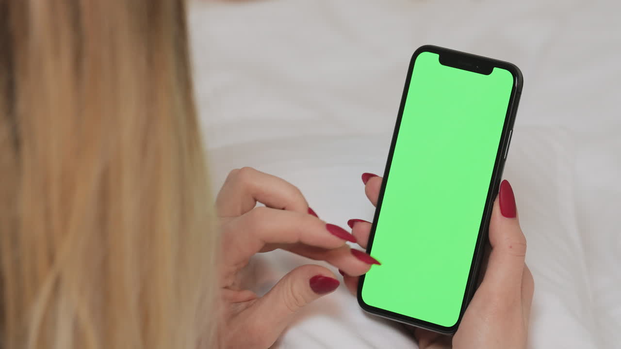 Woman using a phone with green screen on a bed