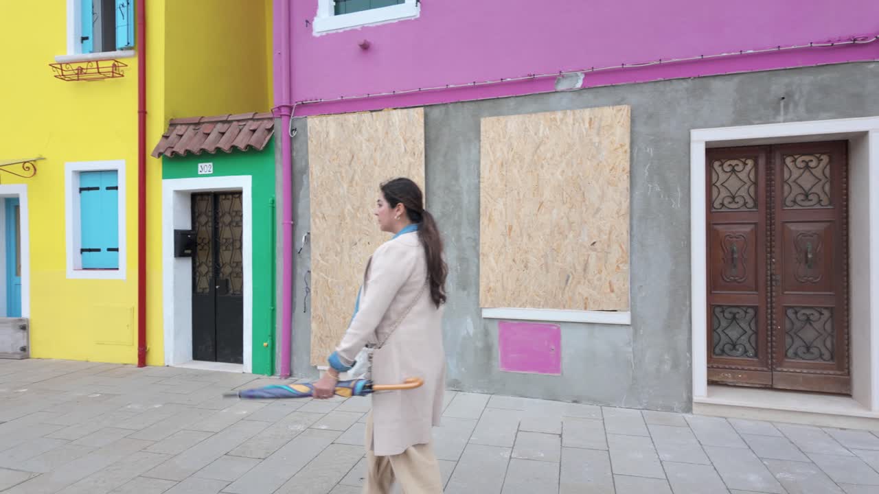 A woman walks past a row of colorful houses in Burano, Italy