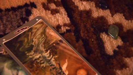 close up of a man's hand using tarot cards one by one, near some stones, on a carpet