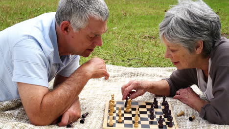 Senior-couple-relaxing-in-the-park-lying-on-a-blanket-playing-chess