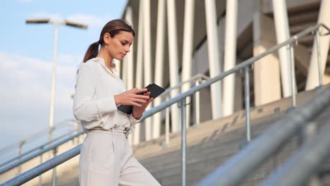 young attractive businesswoman stands on stairs and looks at her tablet