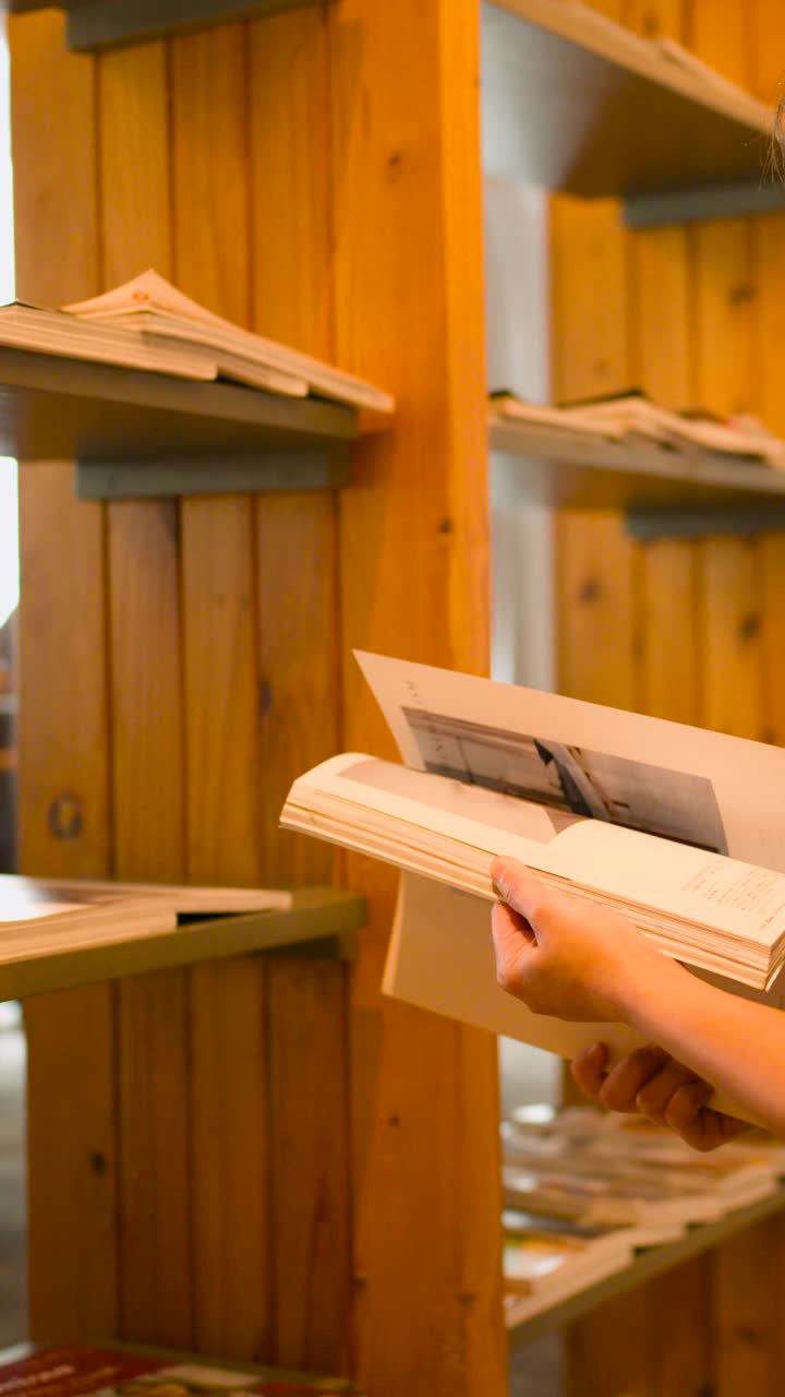 Le mani di una persona sfogliano le pagine di una rivista su uno sfondo di una calda libreria in legno