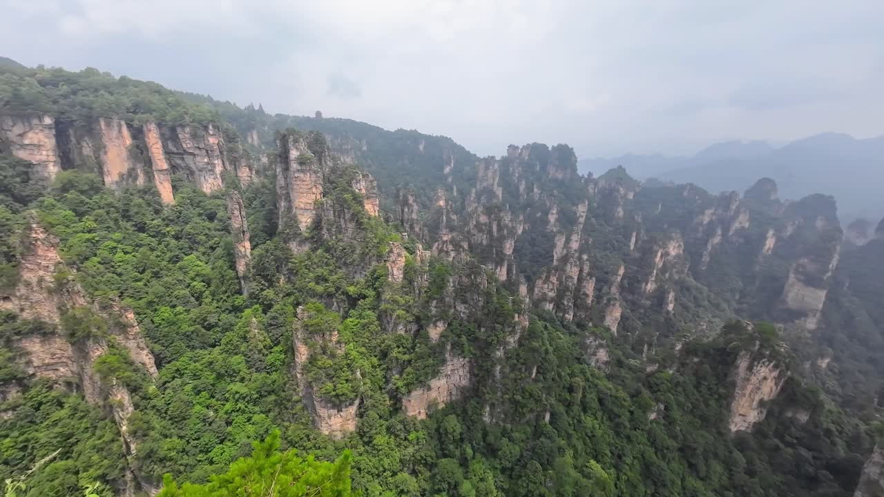 Aerial camera pans left showing dramatic spires of stone covered in forest rising from the Zhangjiajie landscape