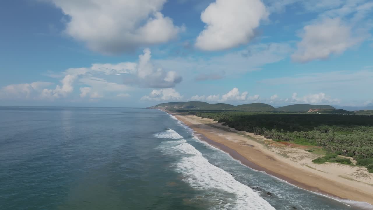 Un drone si alza per rivelare la costa incontaminata della spiaggia di Rambilli, con dietro foreste e colline, in Andhra Pradesh, India.