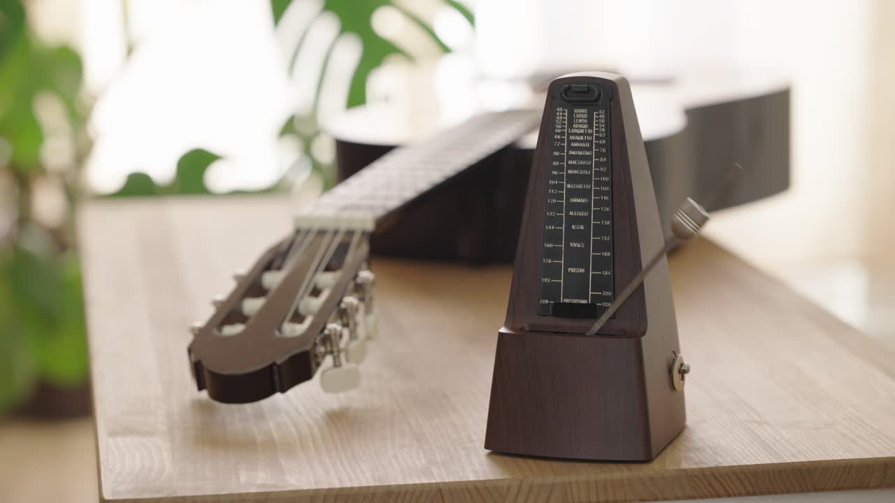 Metronome and acoustic guitar on wooden table in sunlight