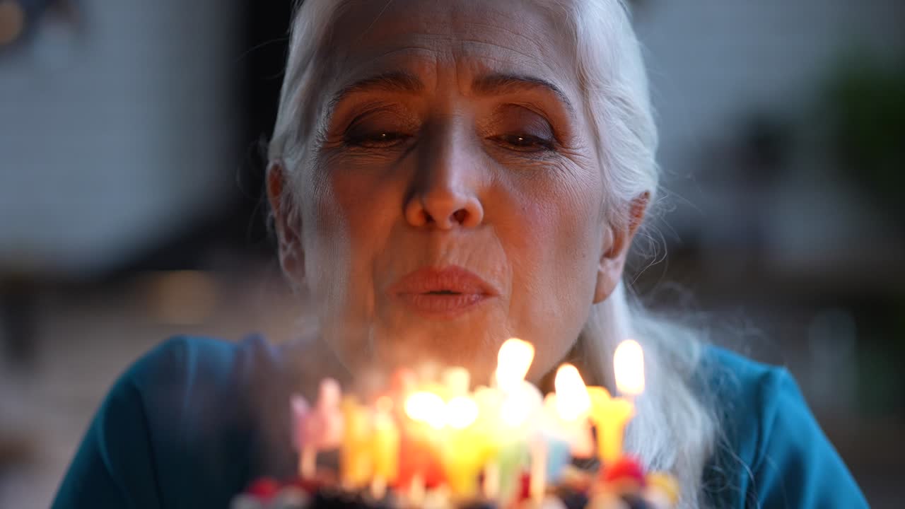 Smiling aged Birthday girl blowing candles on cake