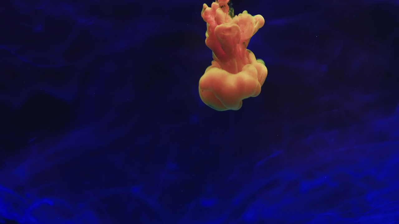 파란색 배경을 배경으로 물에  ⁇ 이는 분홍색과 노란색 수채화 잉크의 느린 동작 비디오