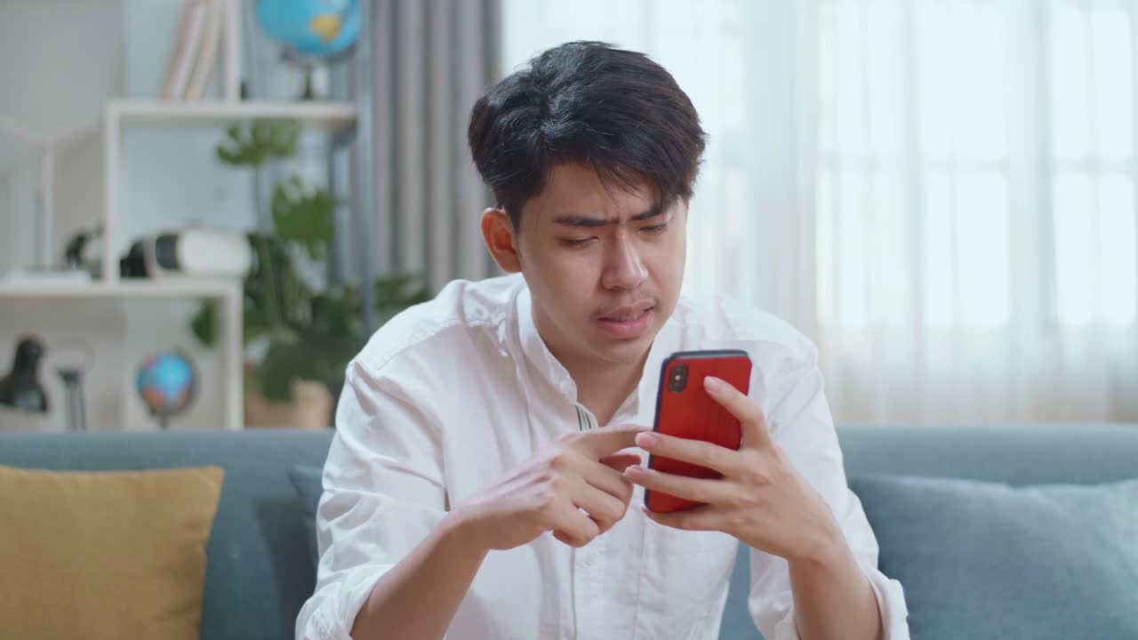 Asian Man Being Tired While Using Smartphone In The Living Room