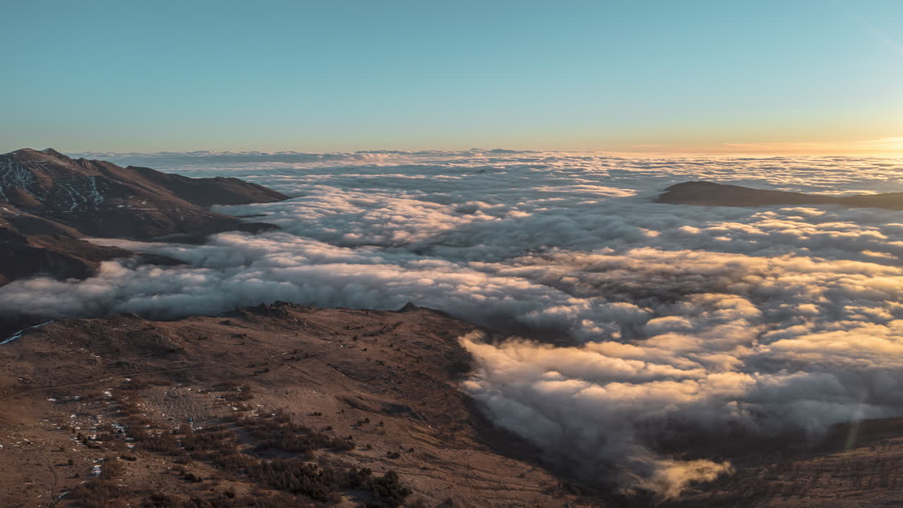 Sunrise over mountains with clouds flowing like a river in the valley, aerial view, timelapse