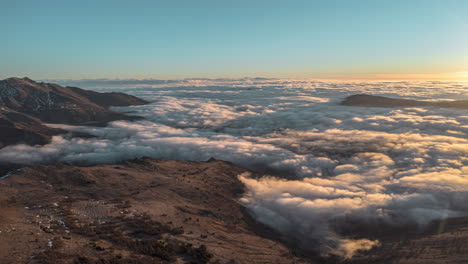 Sunrise-over-mountains-with-clouds-flowing-like-a-river-in-the-valley,-aerial-view,-timelapse