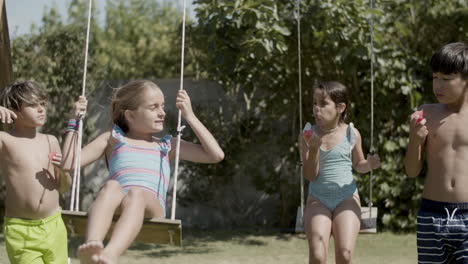 Children-relaxing-at-backyard-playground,-swinging-and-talking.