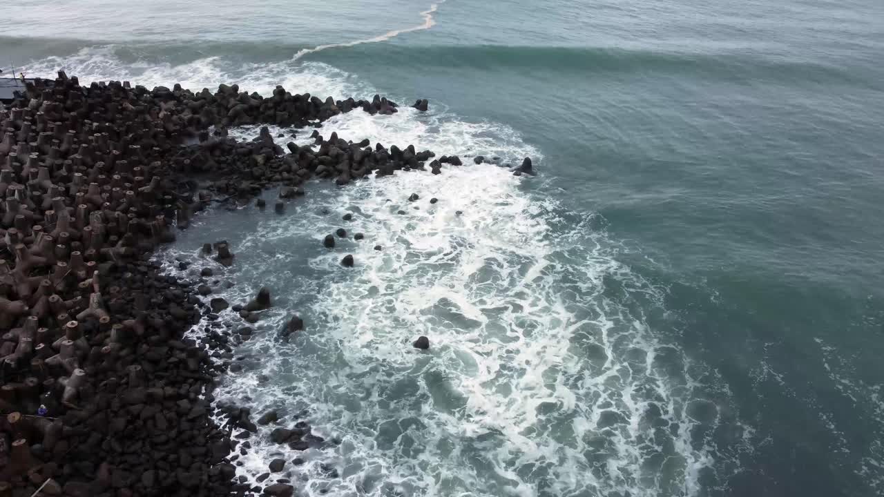 vista aérea de las olas del mar rompiendo bloques de tetra concreto o piedra rompeolas en la playa de glagah, indonesia por la mañana