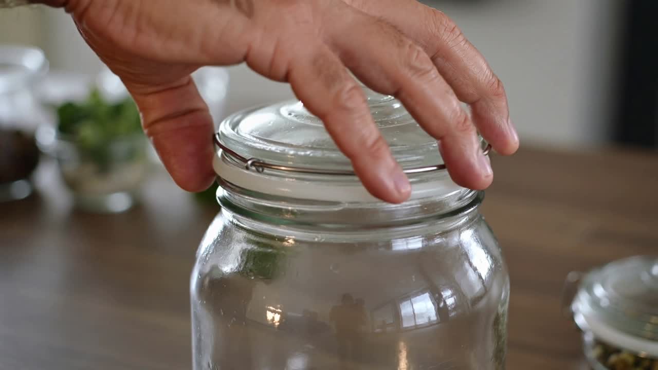 Lowering man's hand placing glass lid and fastening metal clamp on kitchen countertop to seal jar