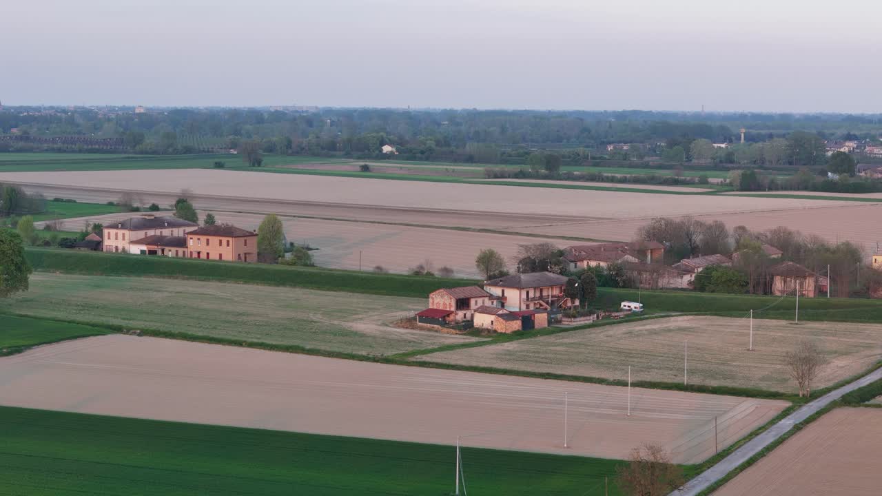 Un drone sorvola la Pianura Padana vicino a Piacenza, mostrando campi coltivati, case coloniche e i corsi d'acqua del fiume Po, catturando le texture rurali, i toni stagionali e il ritmo agricolo dell'Italia settentrionale
