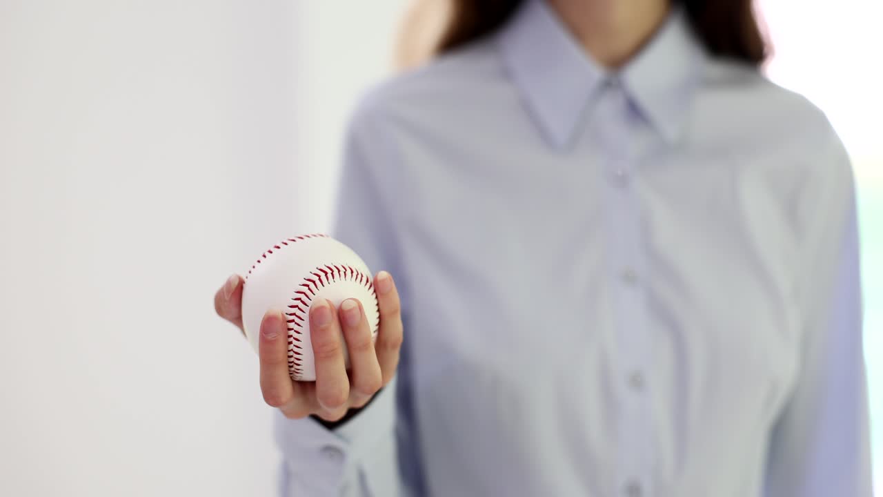 Mano di una donna d'affari che tiene una palla da baseball su sfondo bianco.